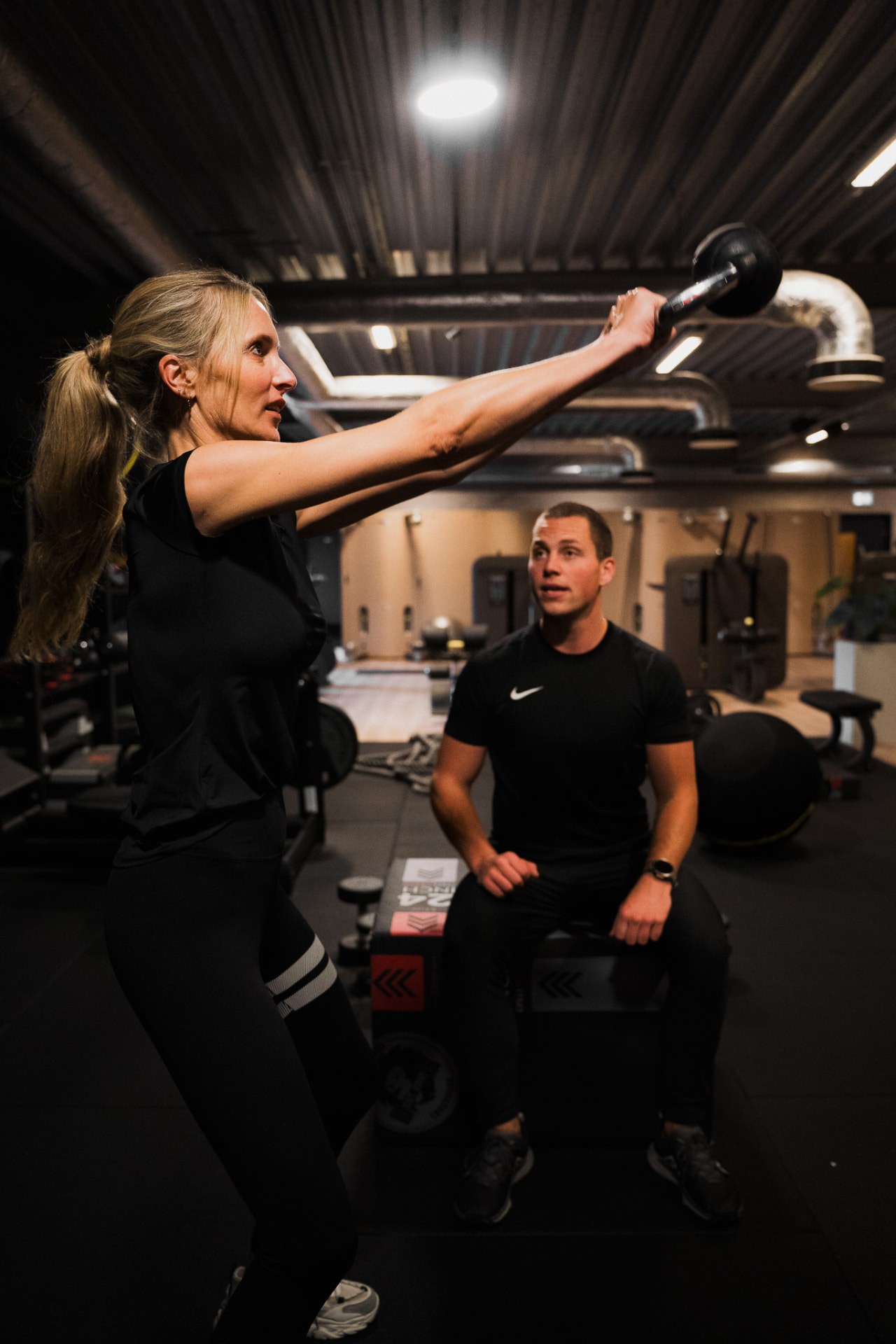 Coach begeleidt een vrouw bij een kettlebell-swing in de gym